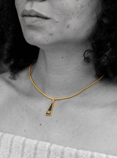 Medalla Inicial "M" de la Serie Triangular en latón con chapado en oro de 18K y esmalte negro.